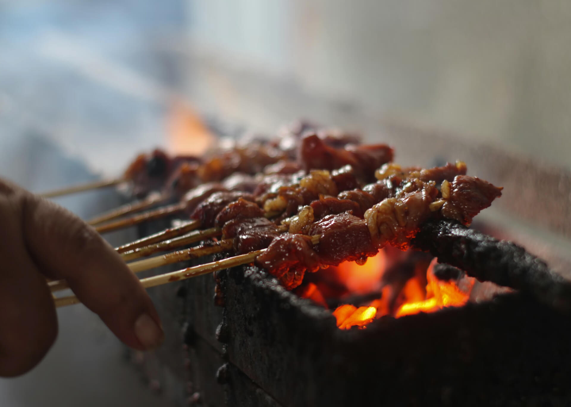 Sate skewers grilling over hot coals with glowing embers